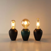 Three handcrafted ceramic cordless lamps in Industrial Rust, Kiln-turned Green, and Matte Black finishes, all lit with different Edison bulbs