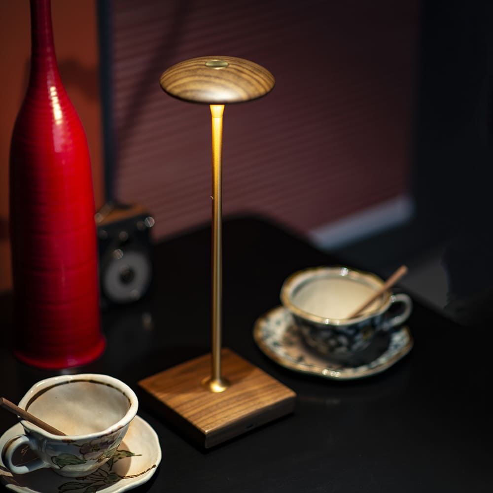 Cordless LED Table Lamp - A different angle of the rounded base, with a cup of coffee and a red vase, showing the lamp's use in a cafe or relaxed setting.