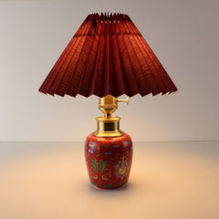 Battery operated ceramic lamp illuminated with warm light, showcasing the portable design and vibrant red pleated shade