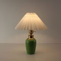 Battery operated green ceramic lamp with white pleated shade emitting soft light, perfect for bistro atmosphere.