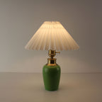 Battery operated green ceramic lamp with white pleated shade emitting soft light, perfect for bistro atmosphere.