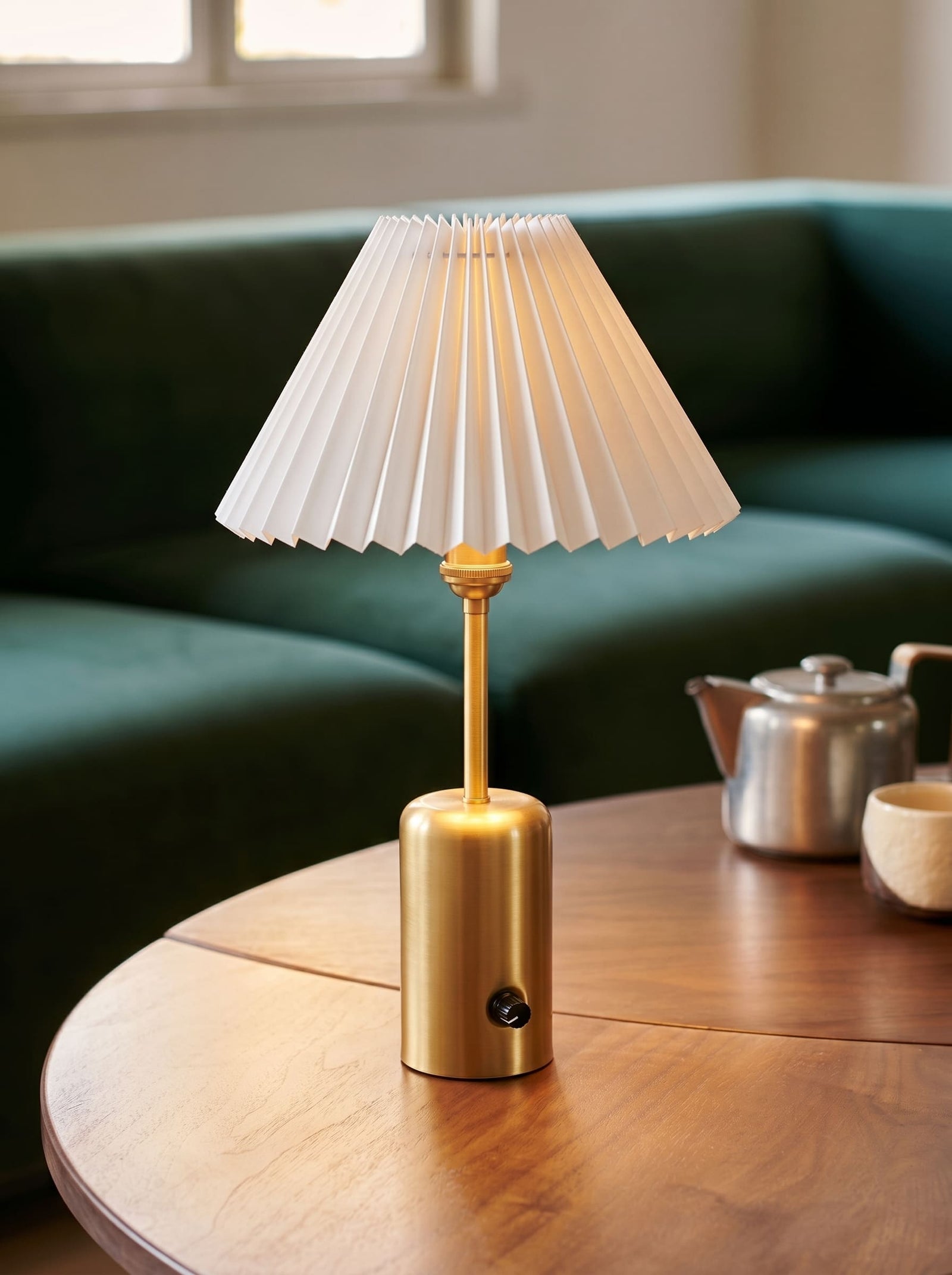 Brass cordless table lamp with a pleated shade styled as bedroom decor on stacked books