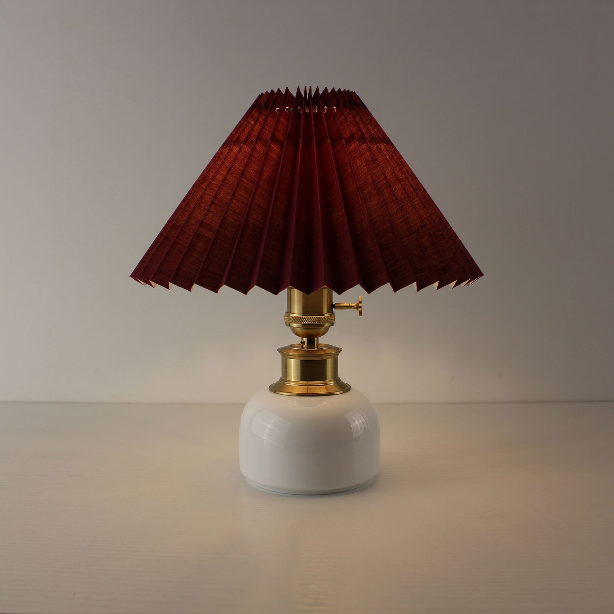 Portable restaurant lamp with burgundy pleated shade, cordless technology, and white ceramic body.