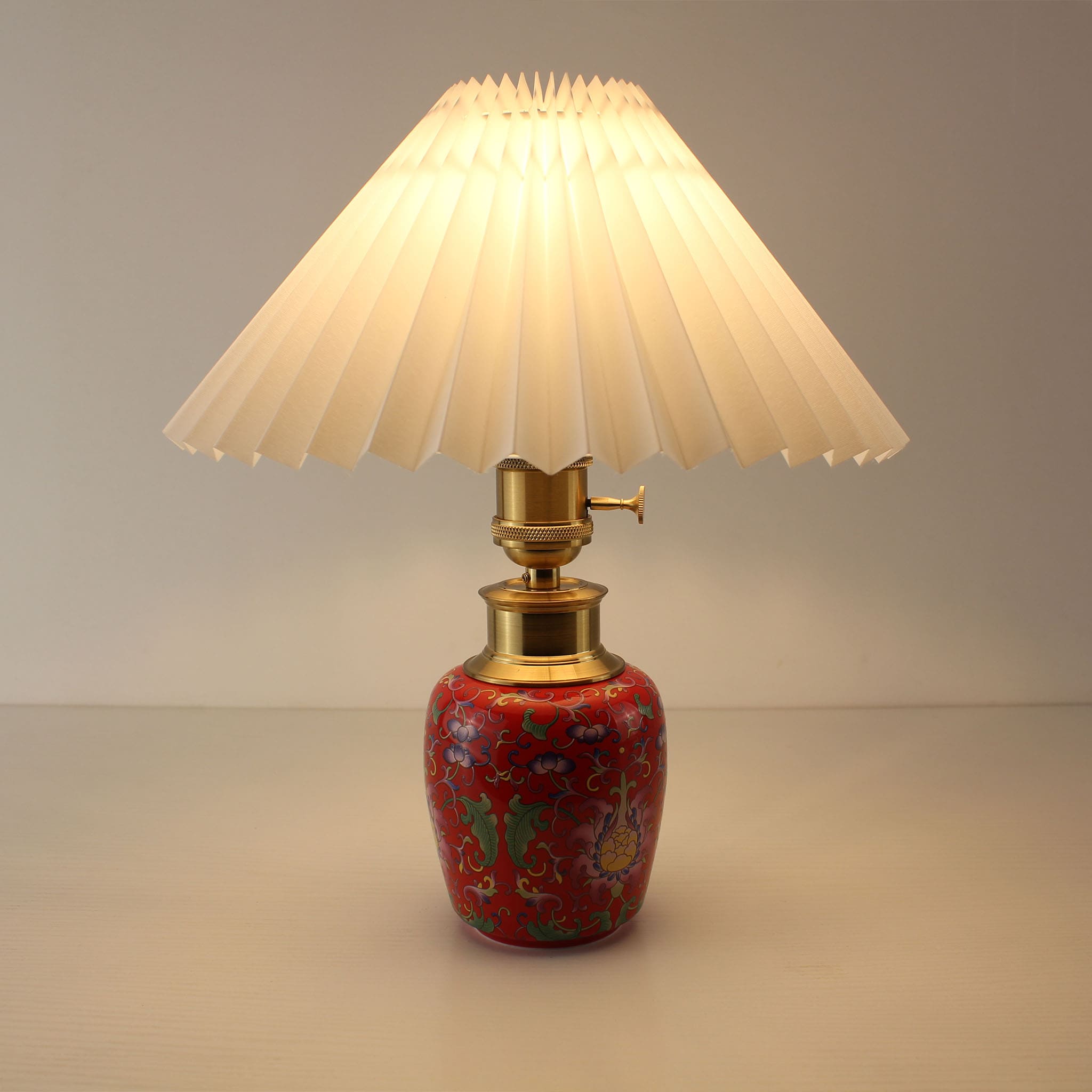 Cordless ceramic table lamp with a white pleated shade and rechargeable battery base, featuring elegant red enamel craftsmanship