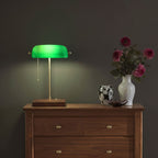 Cordless green bankers lamp with wooden base displayed on a wooden dresser beside decorative flowers