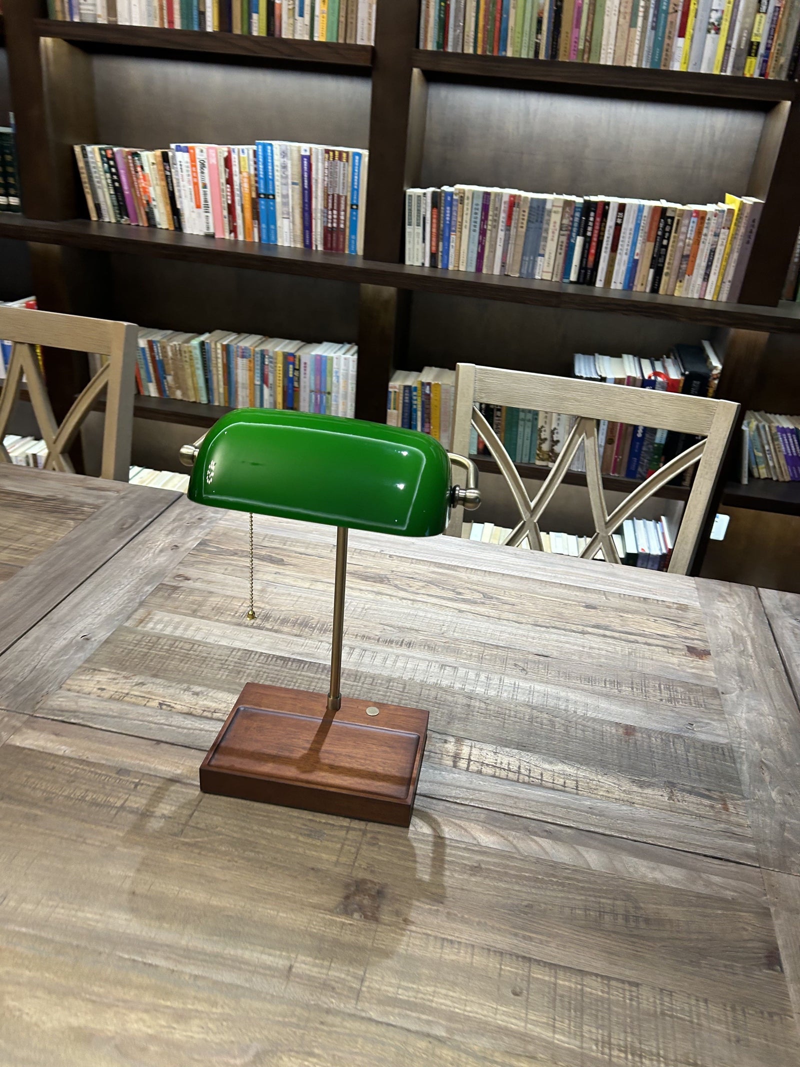 Cordless green bankers lamp with wooden base on a reading table in a library setting