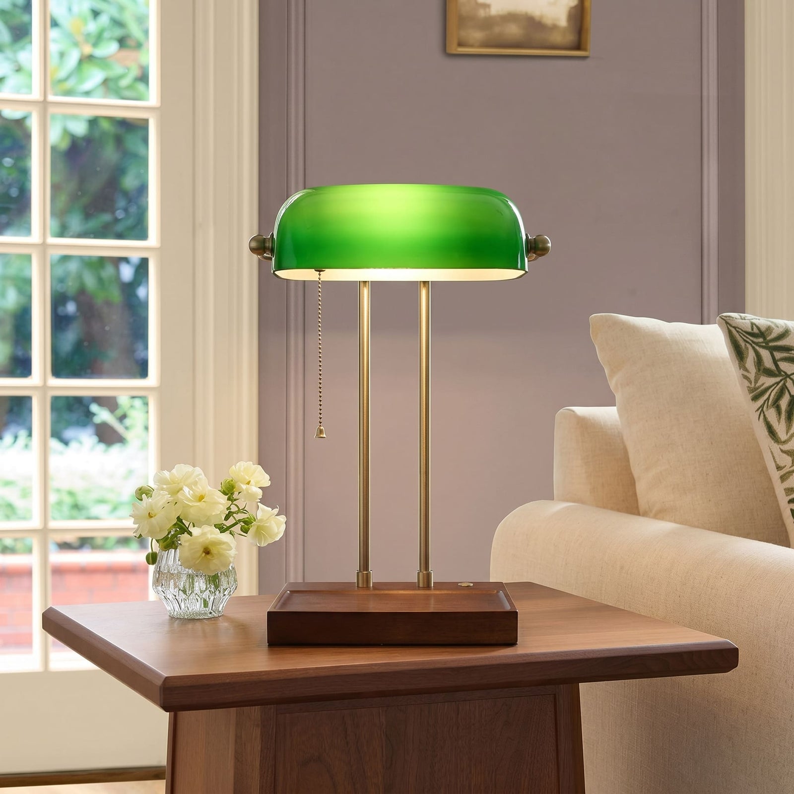 Front view of a cordless green bankers lamp with wooden base on a side table beside a sofa