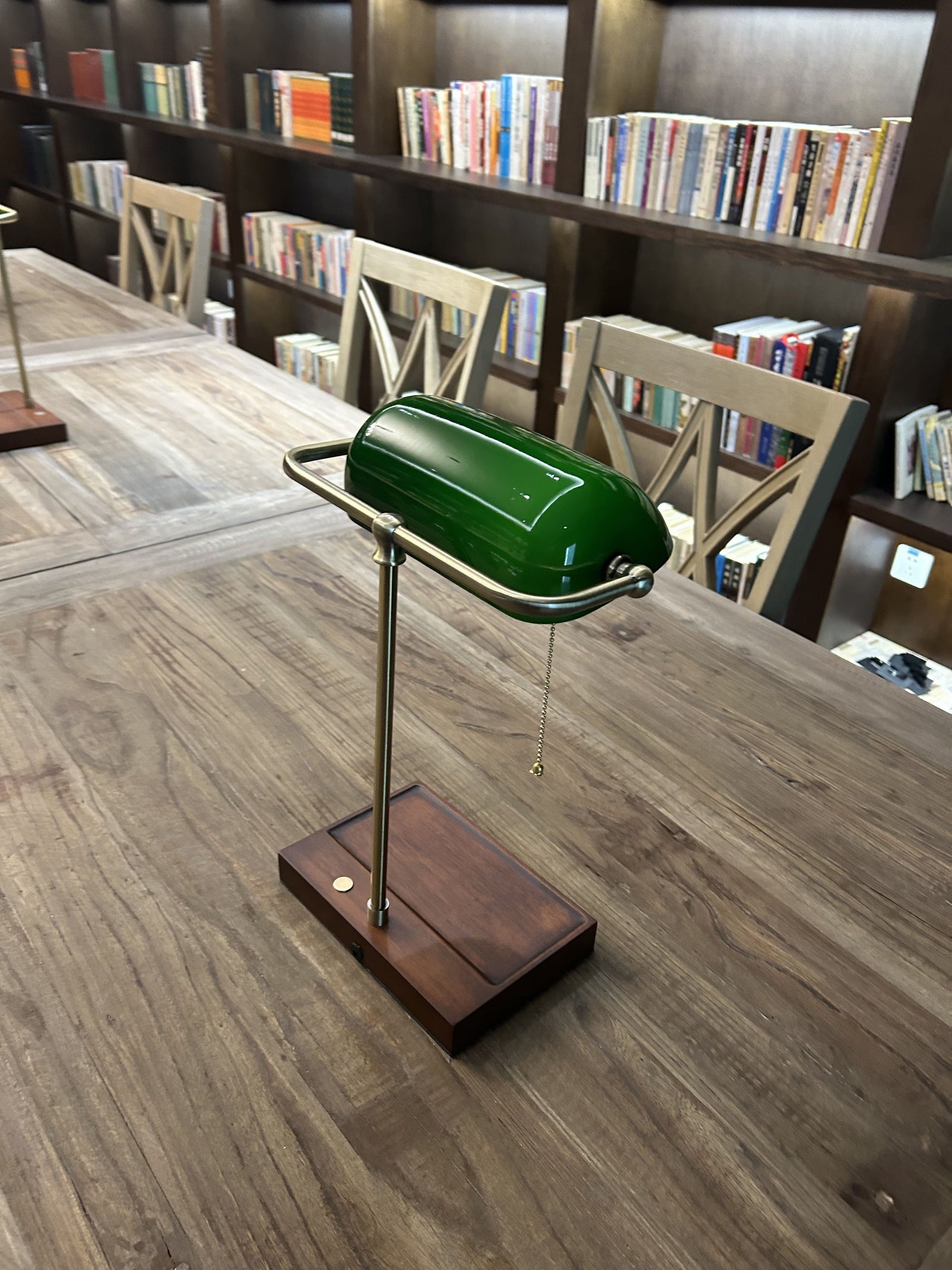 Rear view of a cordless green bankers lamp with wooden base on a library table