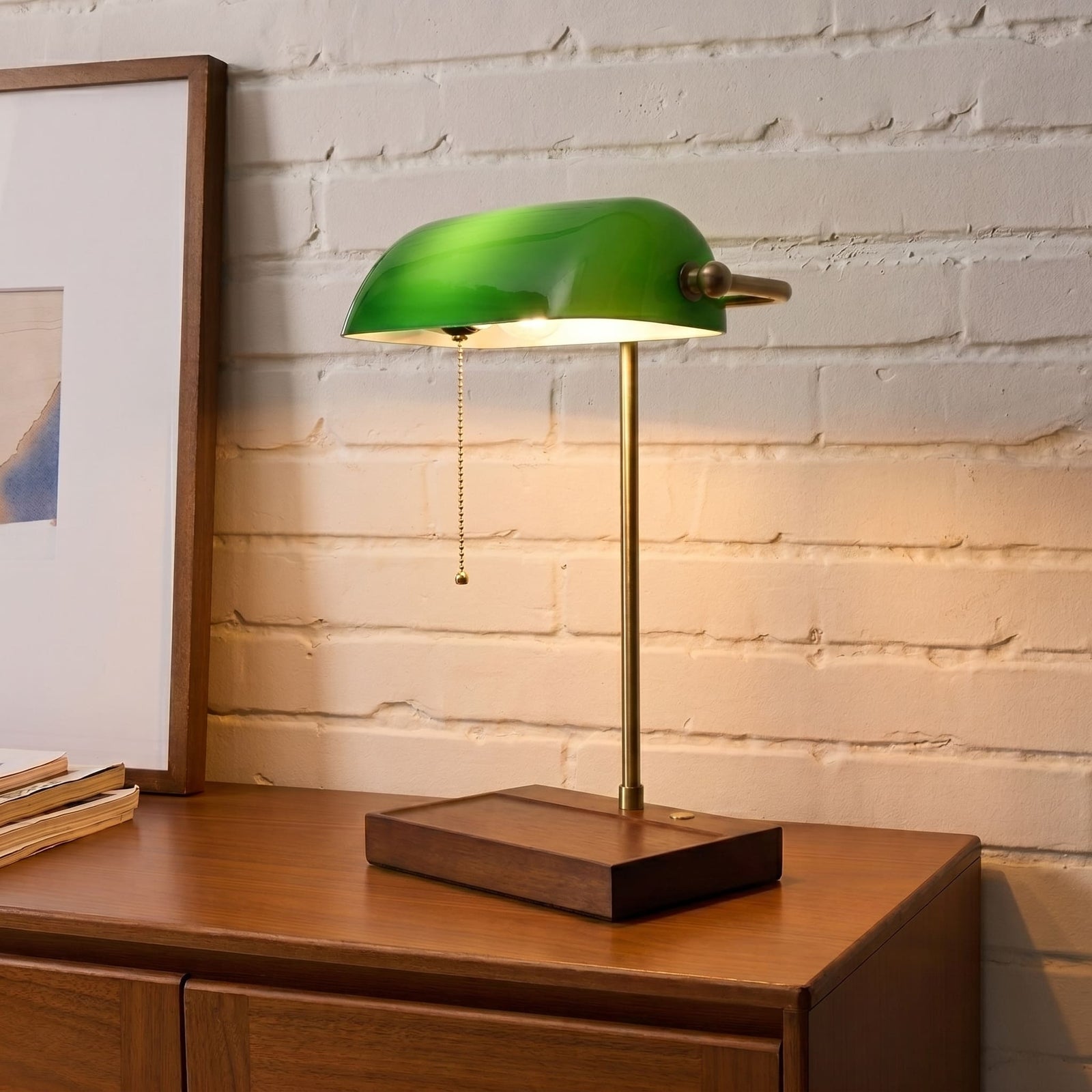 Cordless green bankers lamp with wooden base on a wooden cabinet against a white brick wall