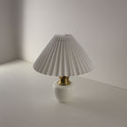 Minimalist cordless porcelain desk lamp with white pleated shade, angled perspective.