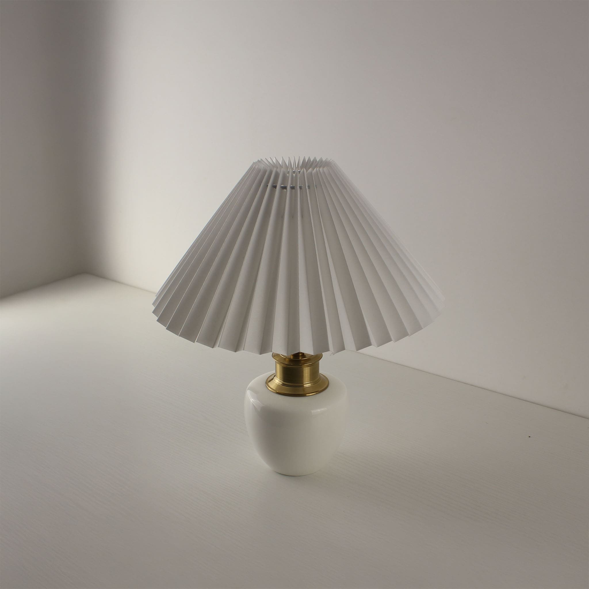 Minimalist cordless porcelain desk lamp with white pleated shade, angled perspective.
