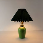 Mid-century modern green ceramic portable lamp with dark green pleated shade illuminated for bedside use.