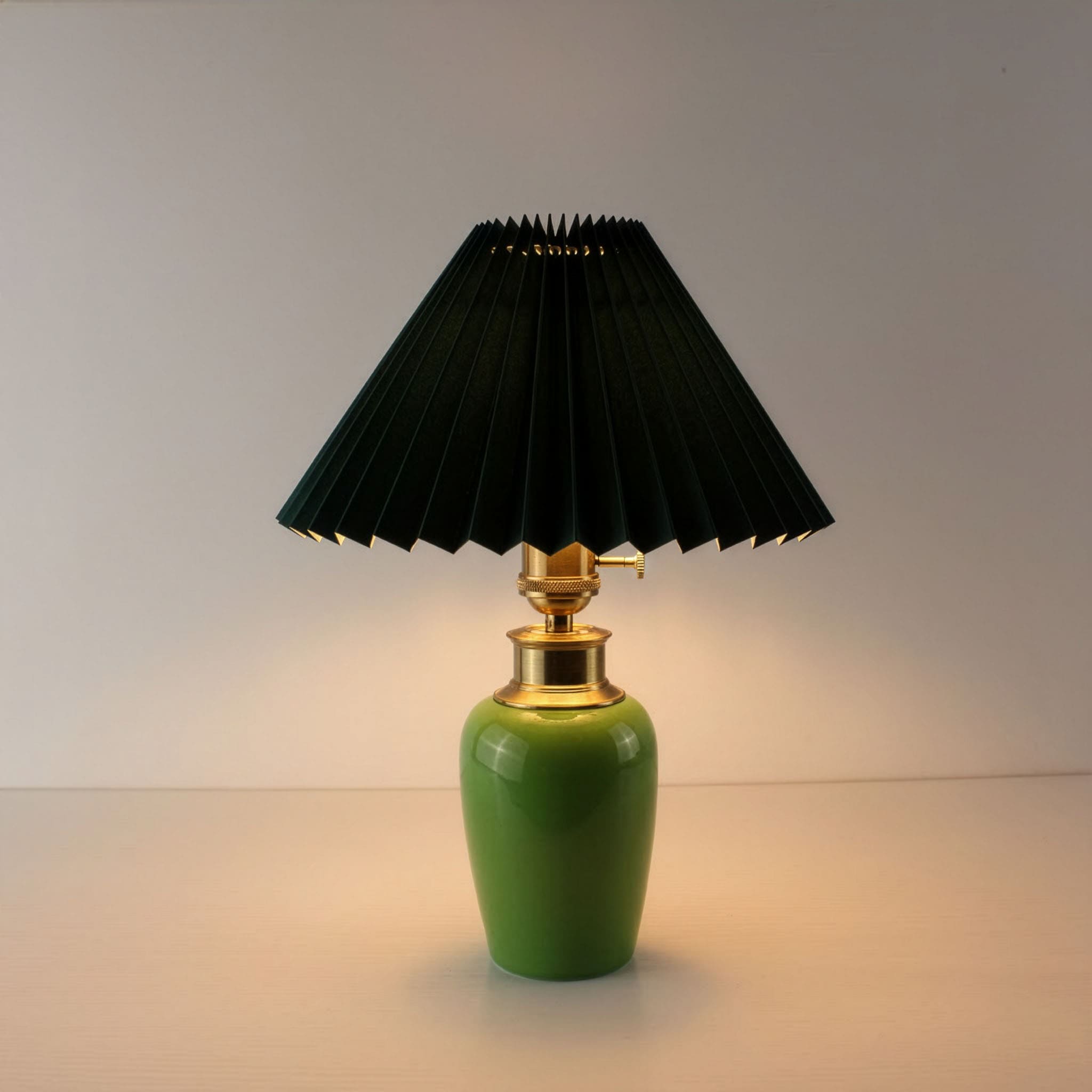 Mid-century modern green ceramic portable lamp with dark green pleated shade illuminated for bedside use.