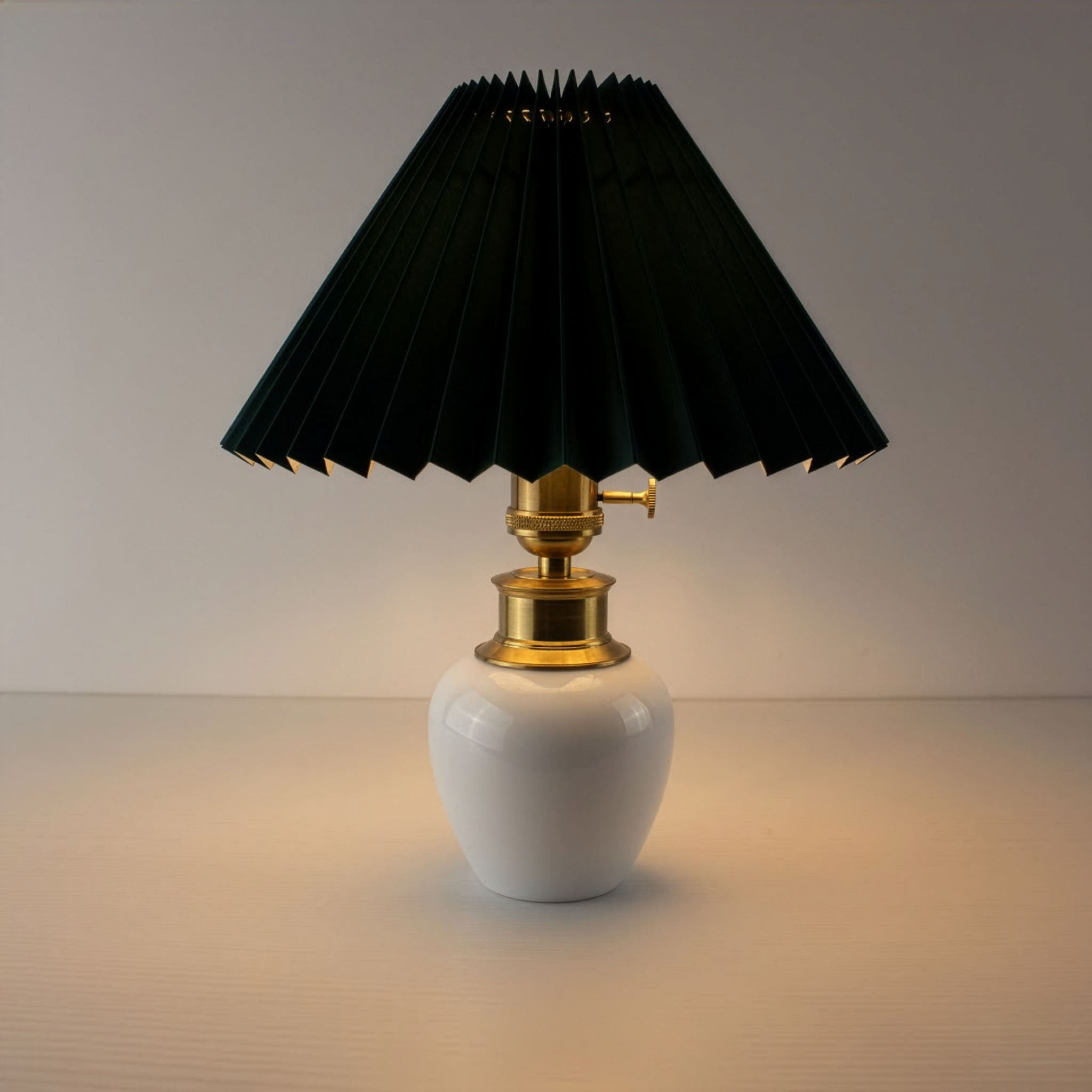 Cordless porcelain table lamp with dark green pleated shade illuminated, providing warm ambient lighting for restaurants.