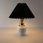 Cordless porcelain table lamp with dark green pleated shade illuminated, providing warm ambient lighting for restaurants.