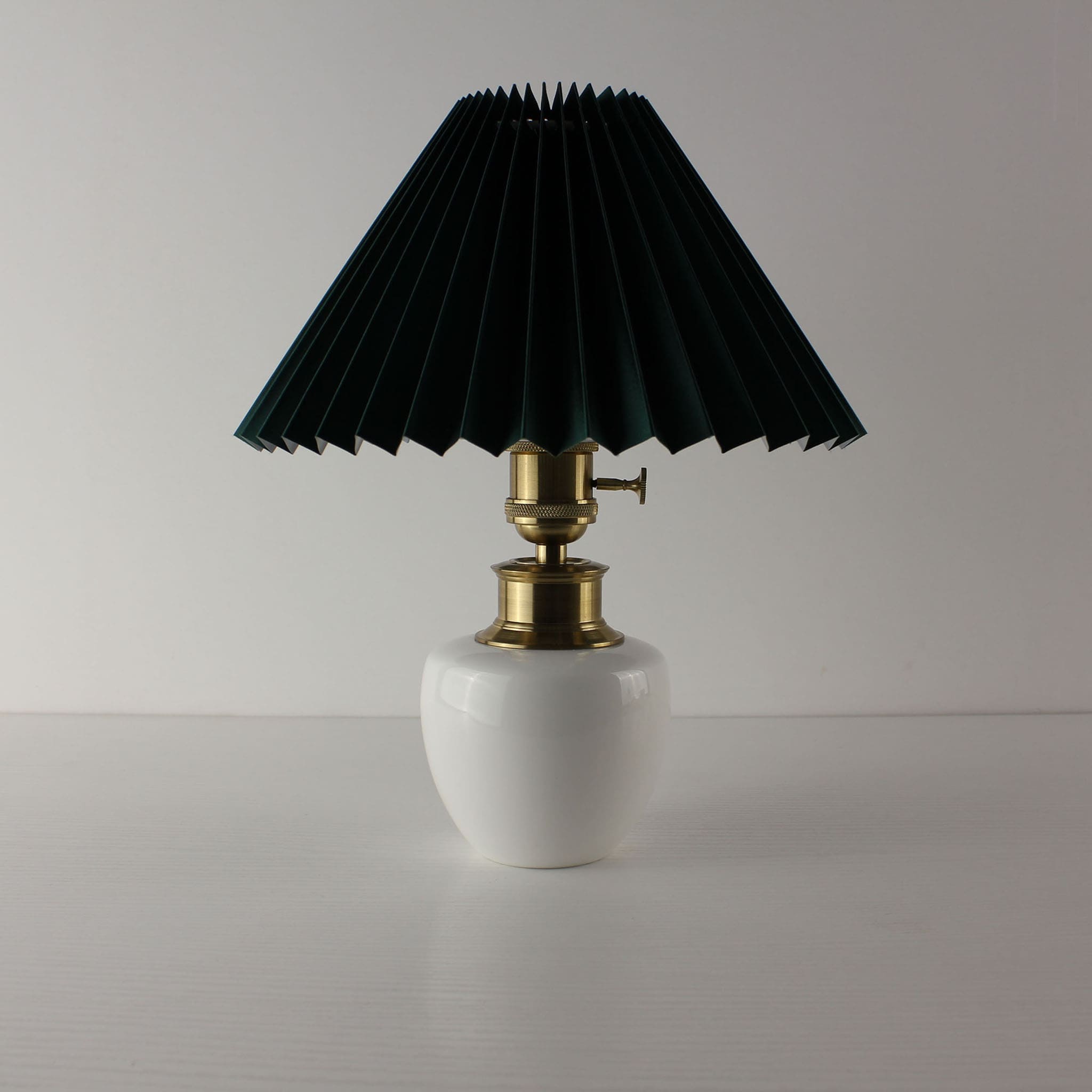 Vintage style porcelain cordless lamp featuring a dark green pleated fabric shade.