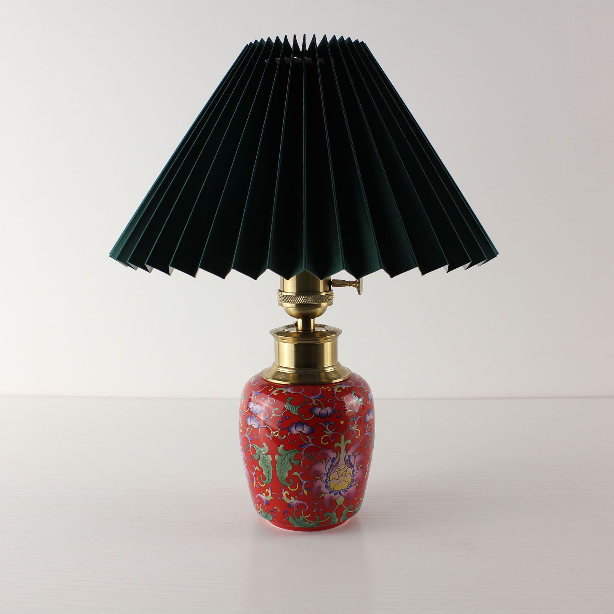 Red enamel ceramic lamp base with a dark green pleated fabric shade, unlit to show the vibrant high-saturation colors