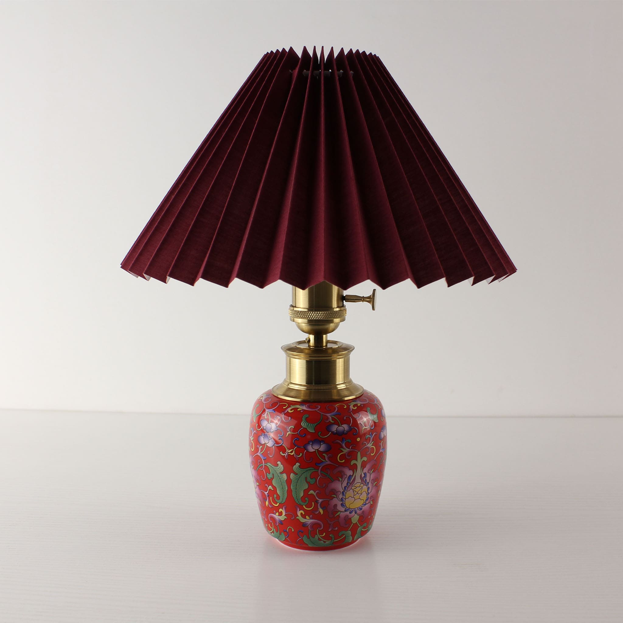 Red enamel ceramic lamp base with a dark green pleated fabric shade, unlit to show the vibrant high-saturation colors