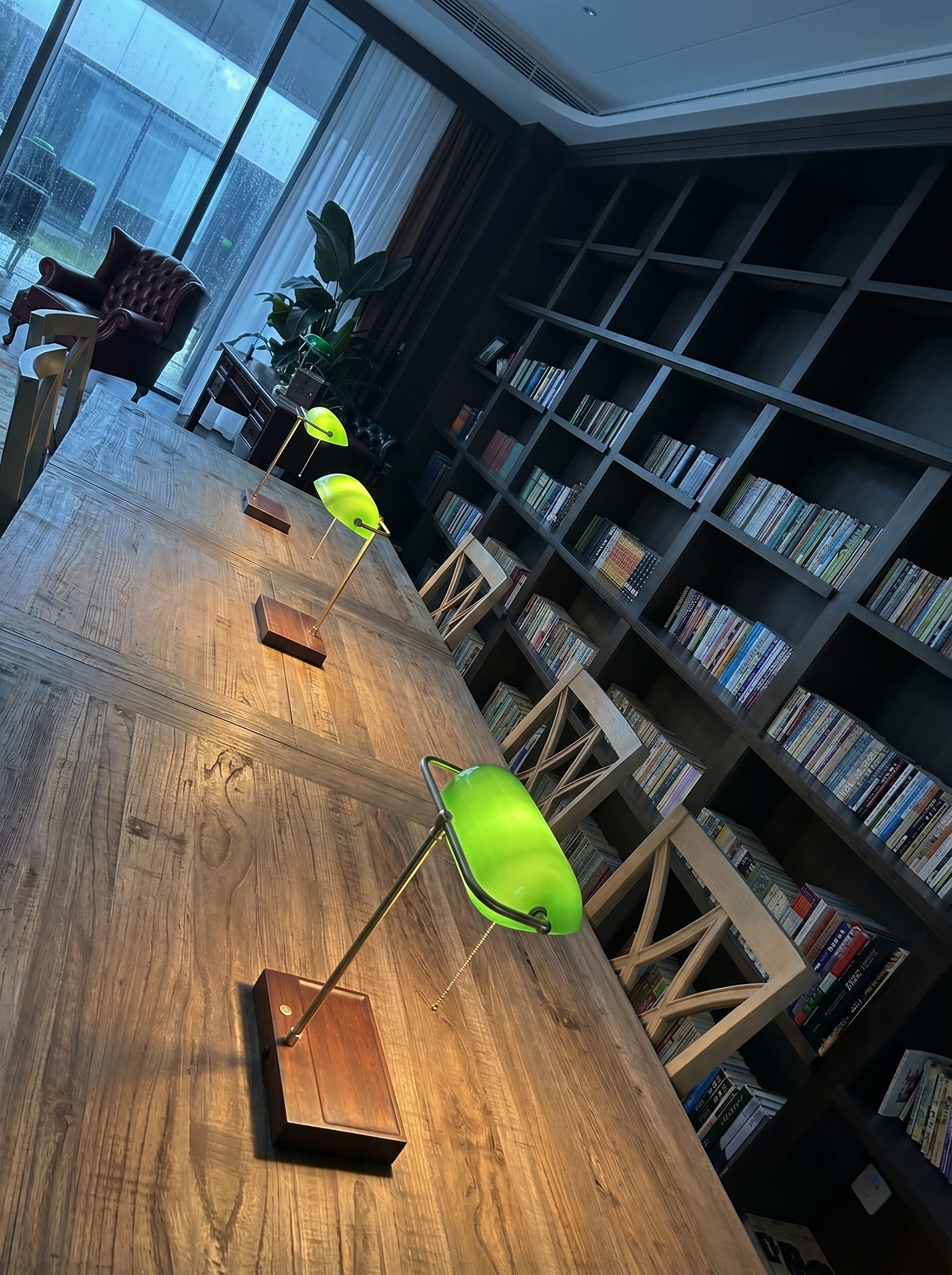 Green glass bankers lamps with wooden bases displayed on a library table from an angled perspective