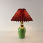 intage green ceramic cordless table lamp with burgundy pleated shade turned on, creating a warm ambient glow.