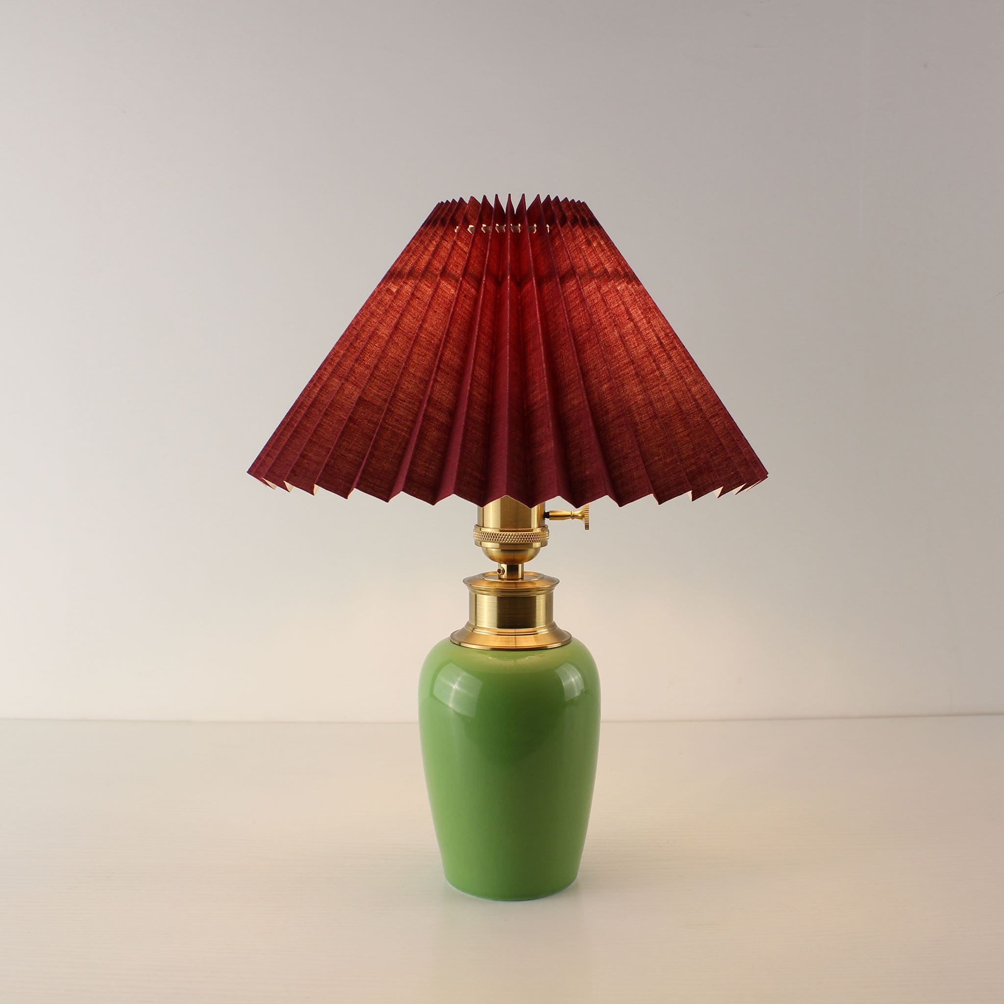 intage green ceramic cordless table lamp with burgundy pleated shade turned on, creating a warm ambient glow.