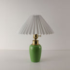 Front view of a MCM green ceramic table lamp with a classic white pleated shade, cordless and portable.