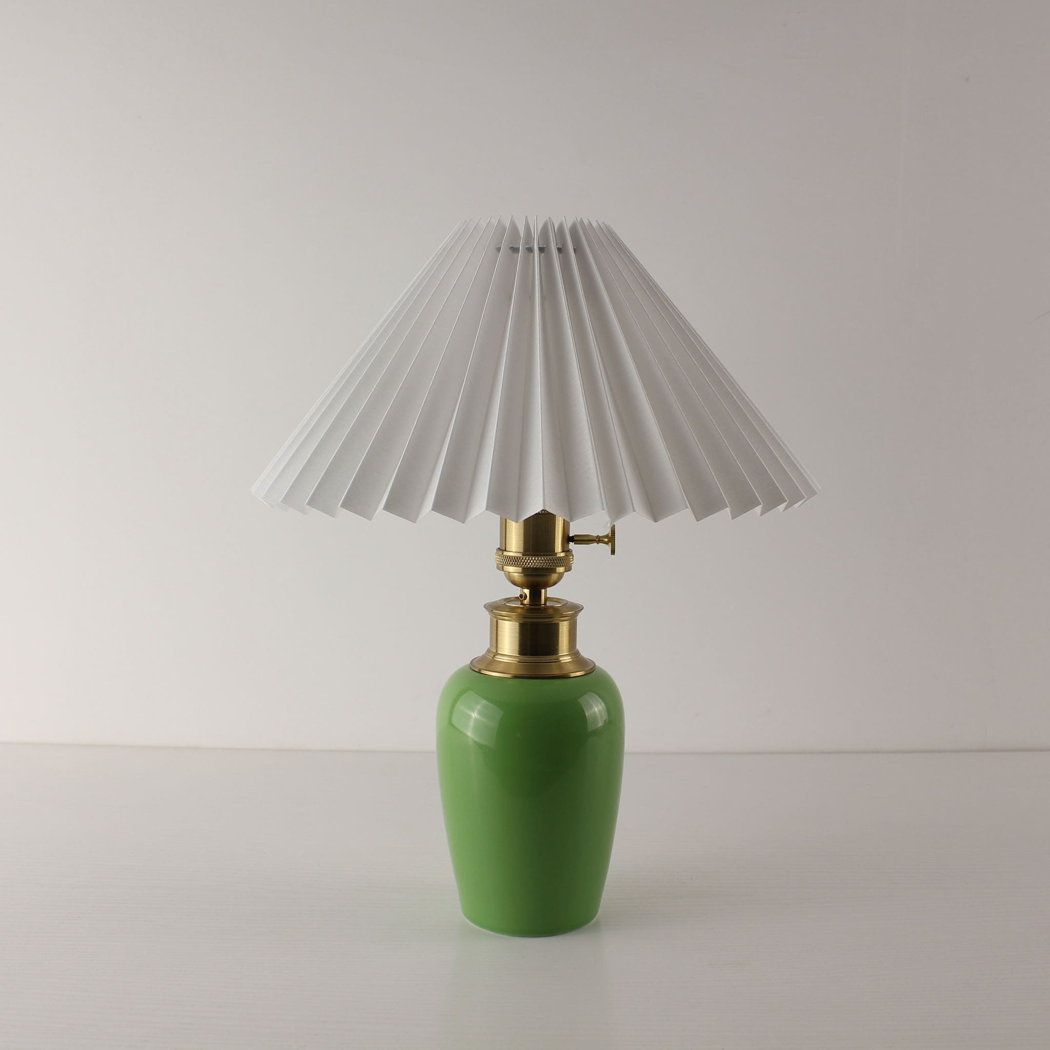 Front view of a MCM green ceramic table lamp with a classic white pleated shade, cordless and portable.