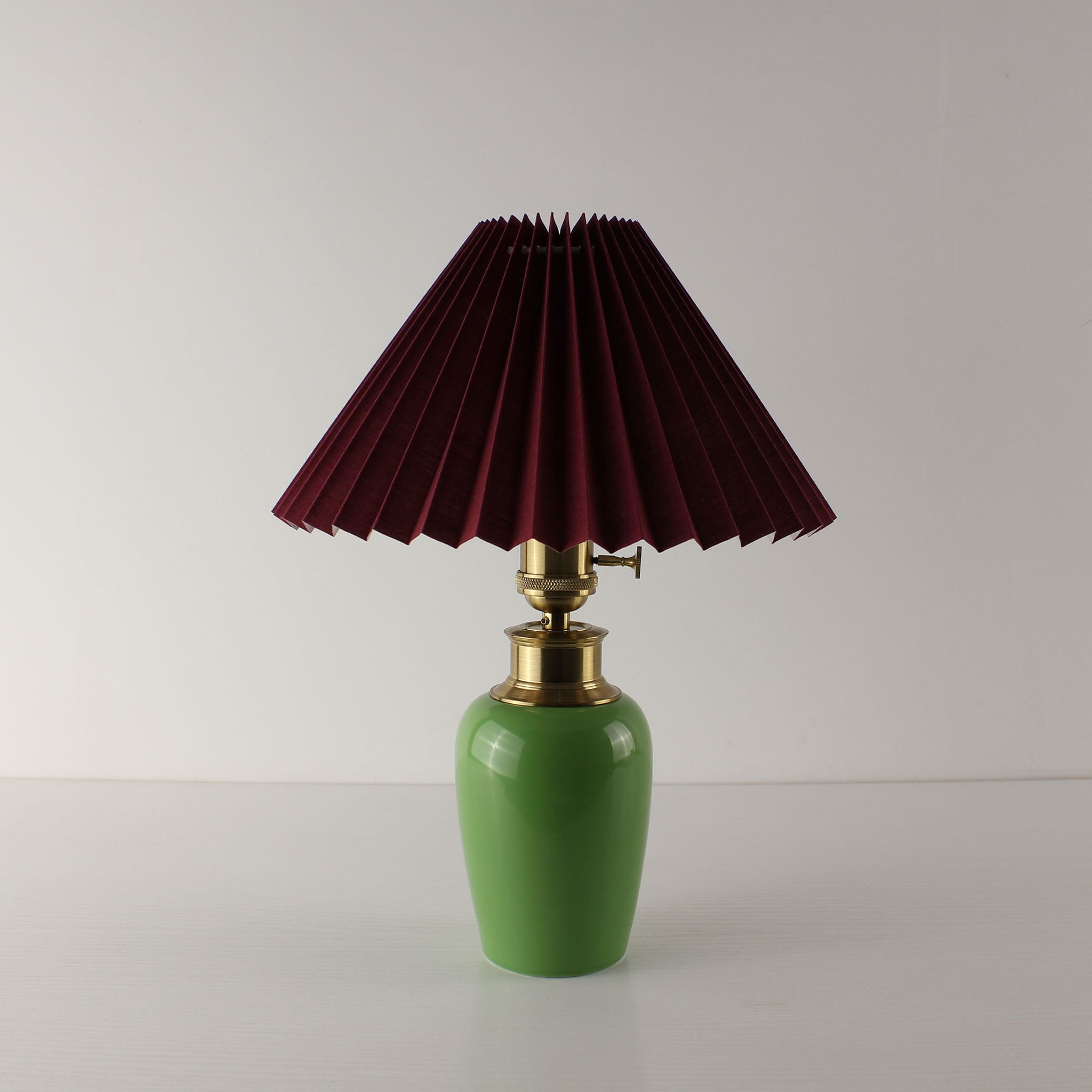 High-end green ceramic rechargeable table lamp with a dark red pleated shade, elegant restaurant decor.