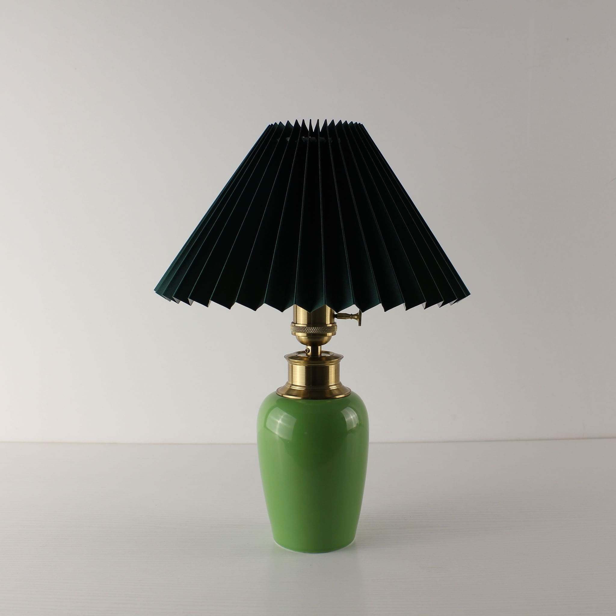 Luxury green ceramic wireless lamp with a forest green pleated shade and brass hardware, vintage MCM style.