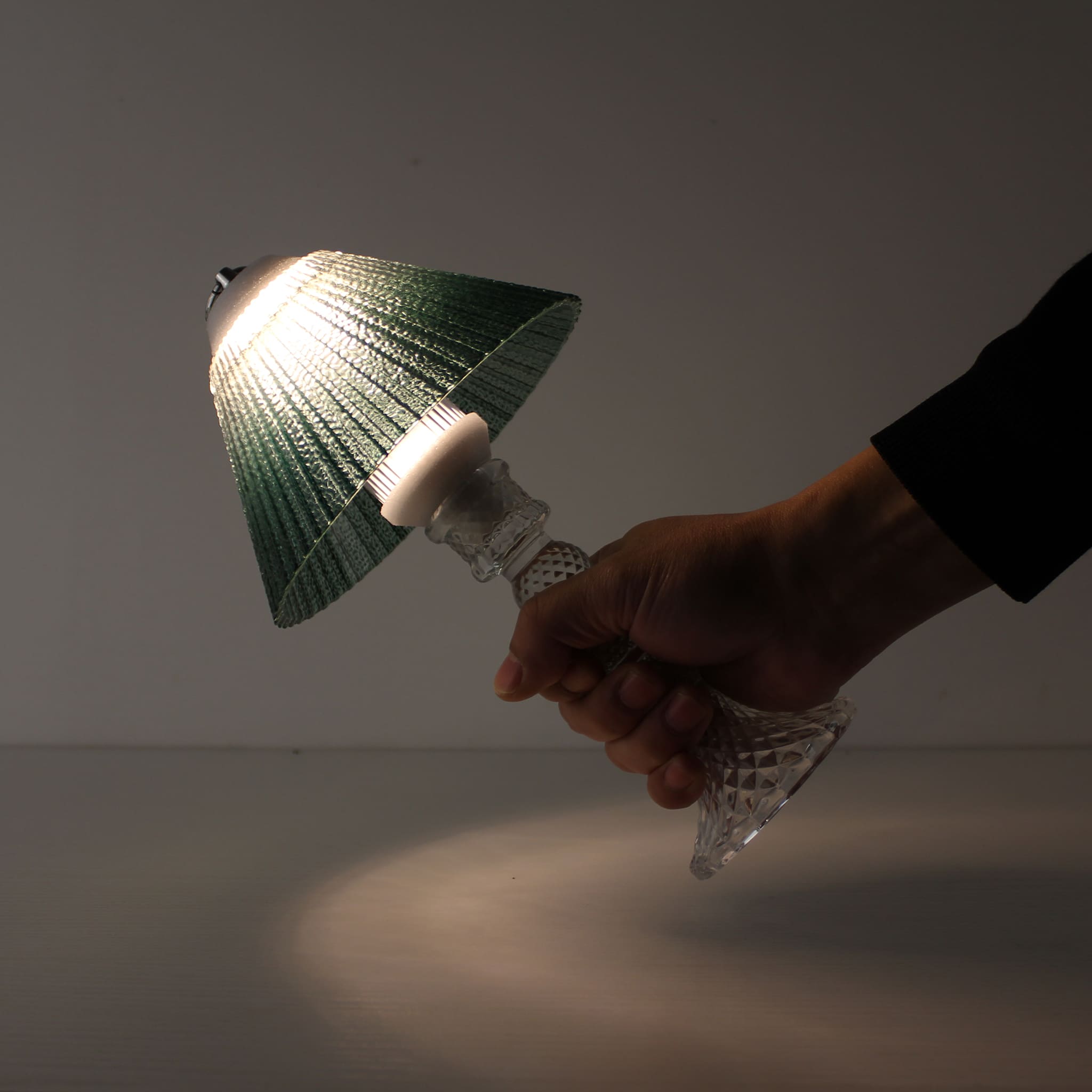 A hand holding the cordless Prism lantern (ON), demonstrating its lightweight and portable battery-powered design.