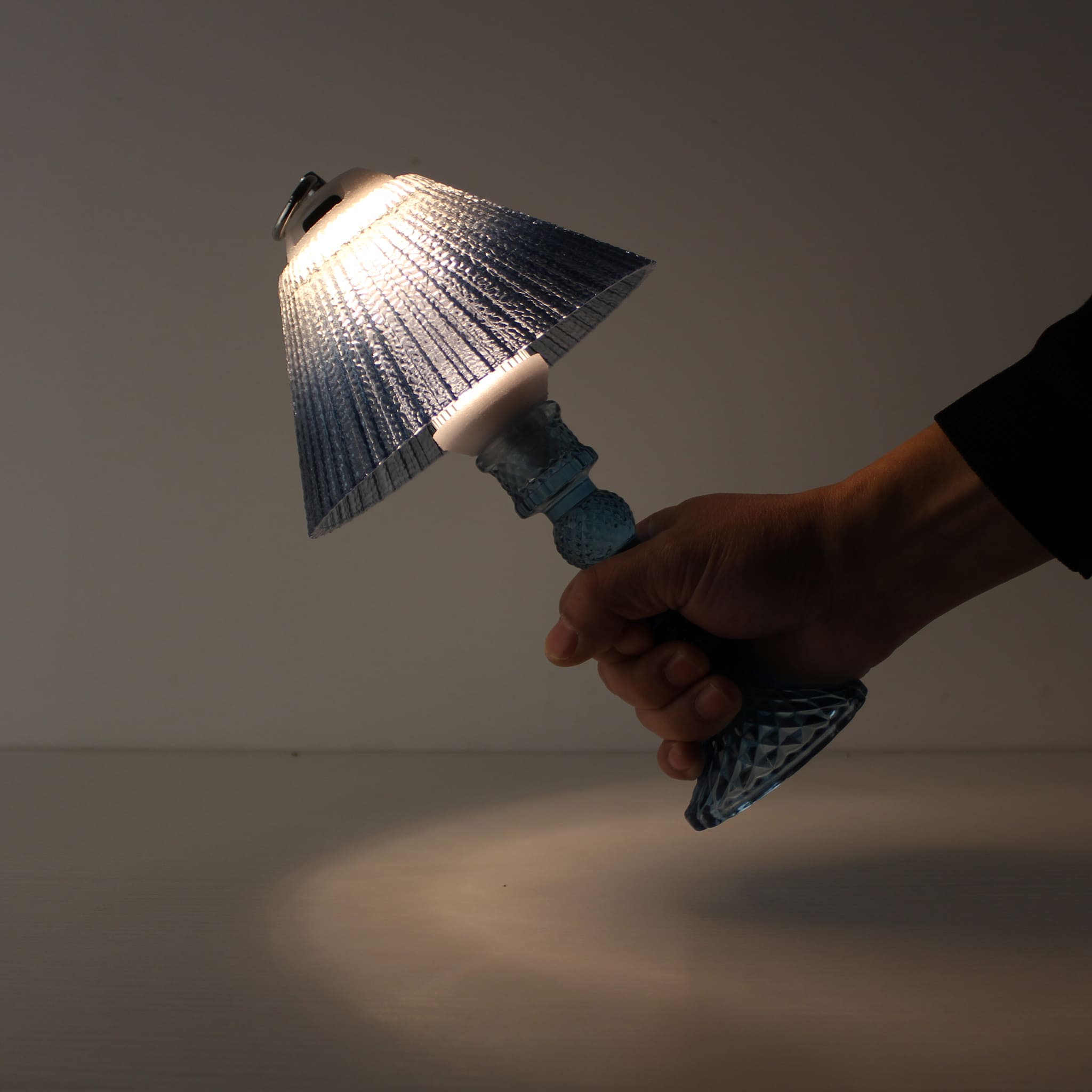 A hand holding the portable blue lantern (ON) by its metal ring, demonstrating cordless mobility and 150h battery runtime.