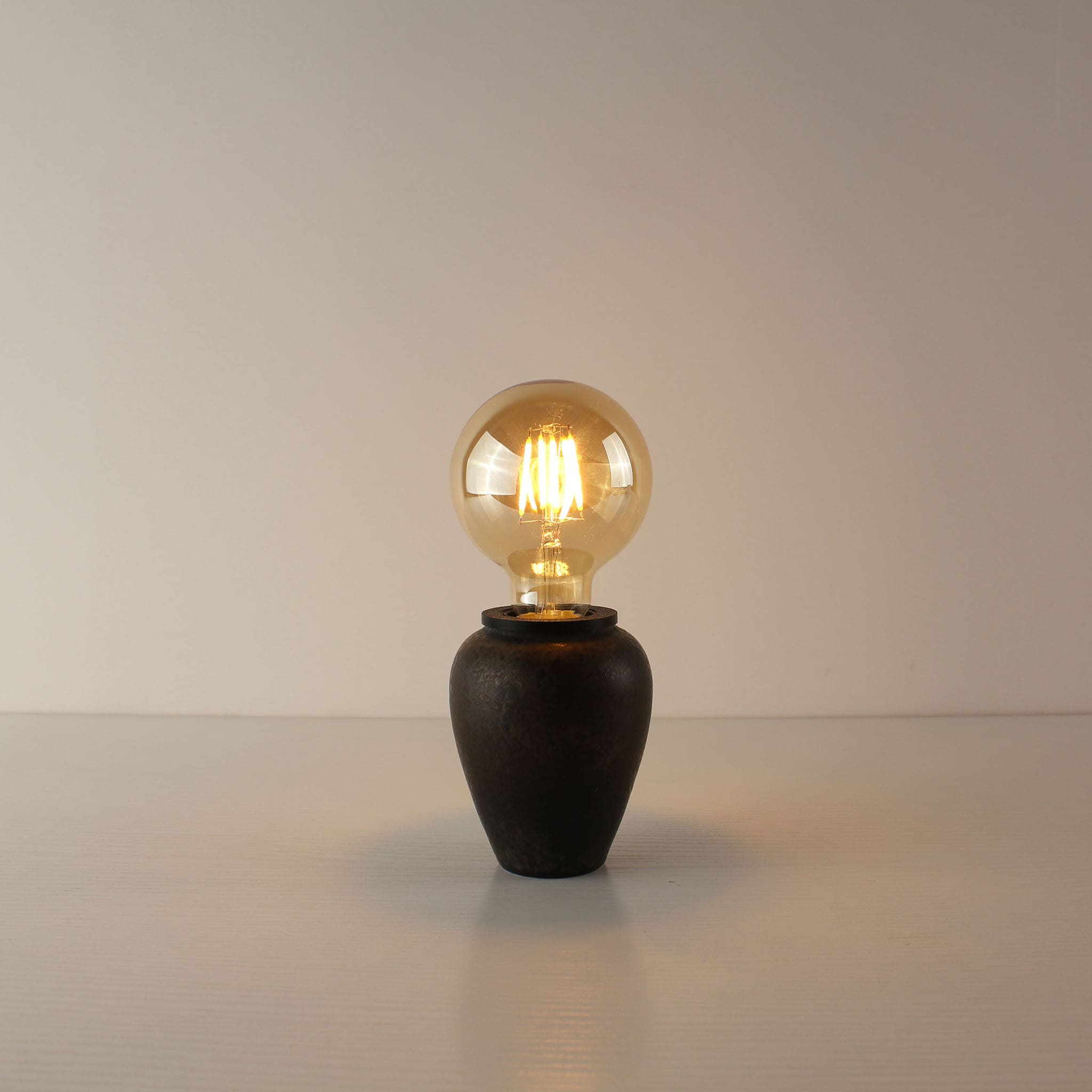 Industrial rust finish ceramic cordless table lamp with a large spherical A80 vintage Edison bulb, emitting a warm ambient glow