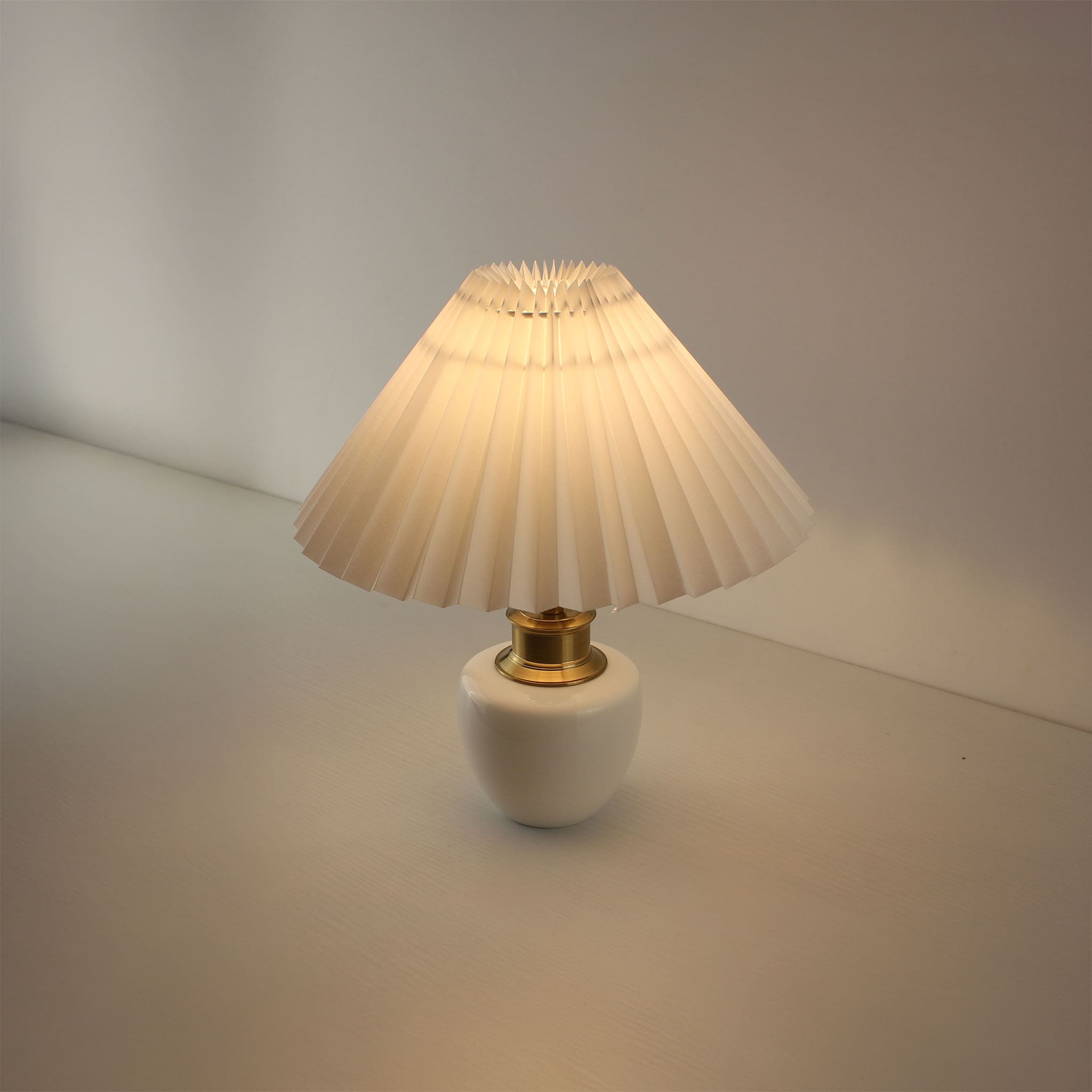 Elegant white pottery rechargeable lamp with light on, showing pleated shade texture.