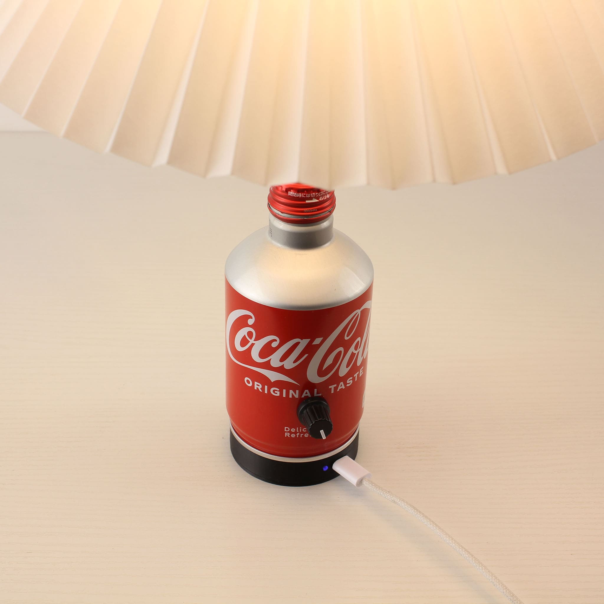 Close-up of the magnetic charging base with a blue indicator light connected to the bottom of the Coca-Cola cordless lamp.