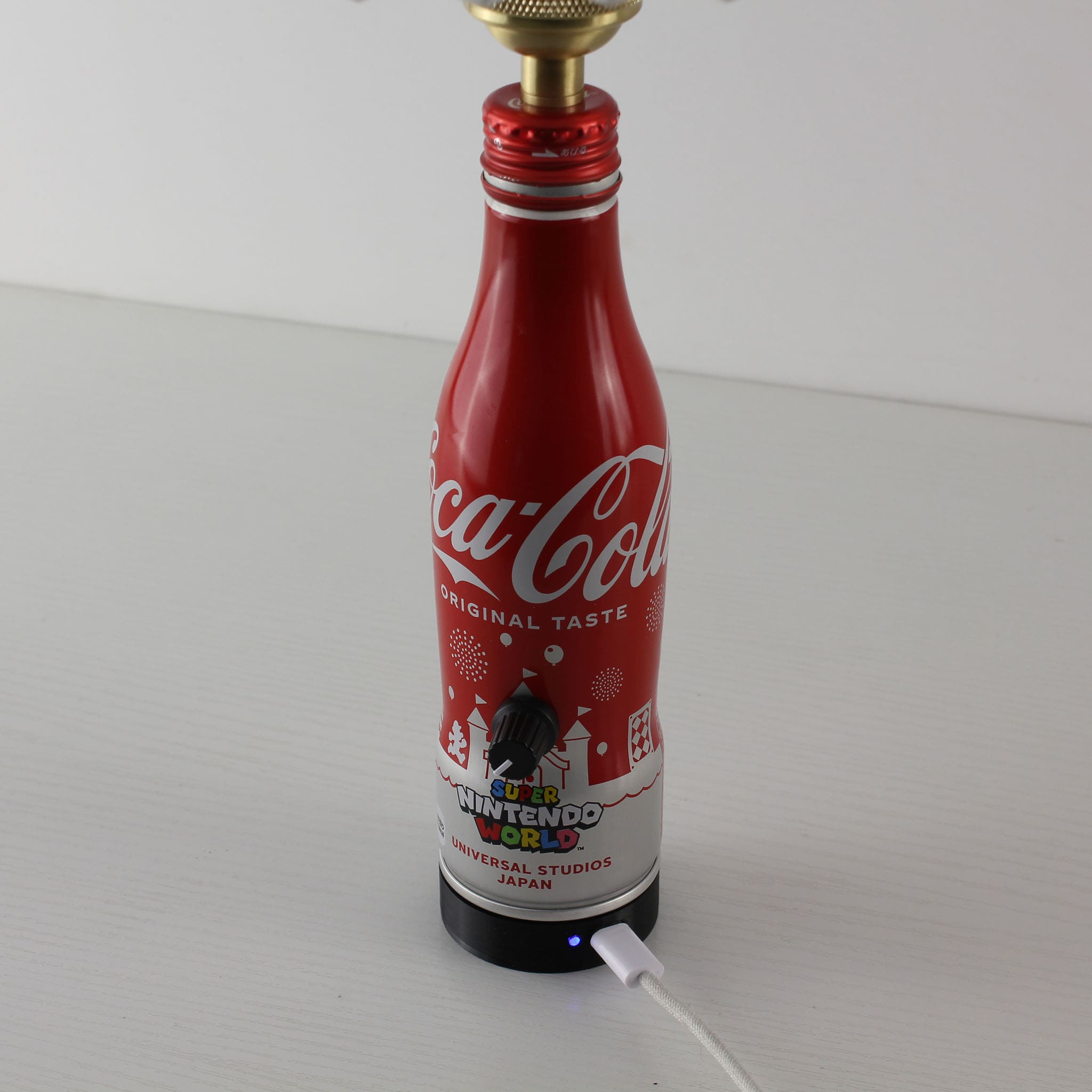 Close-up showing the modern magnetic charging port and Type-C cable connected to the base of the red Coca-Cola bottle lamp
