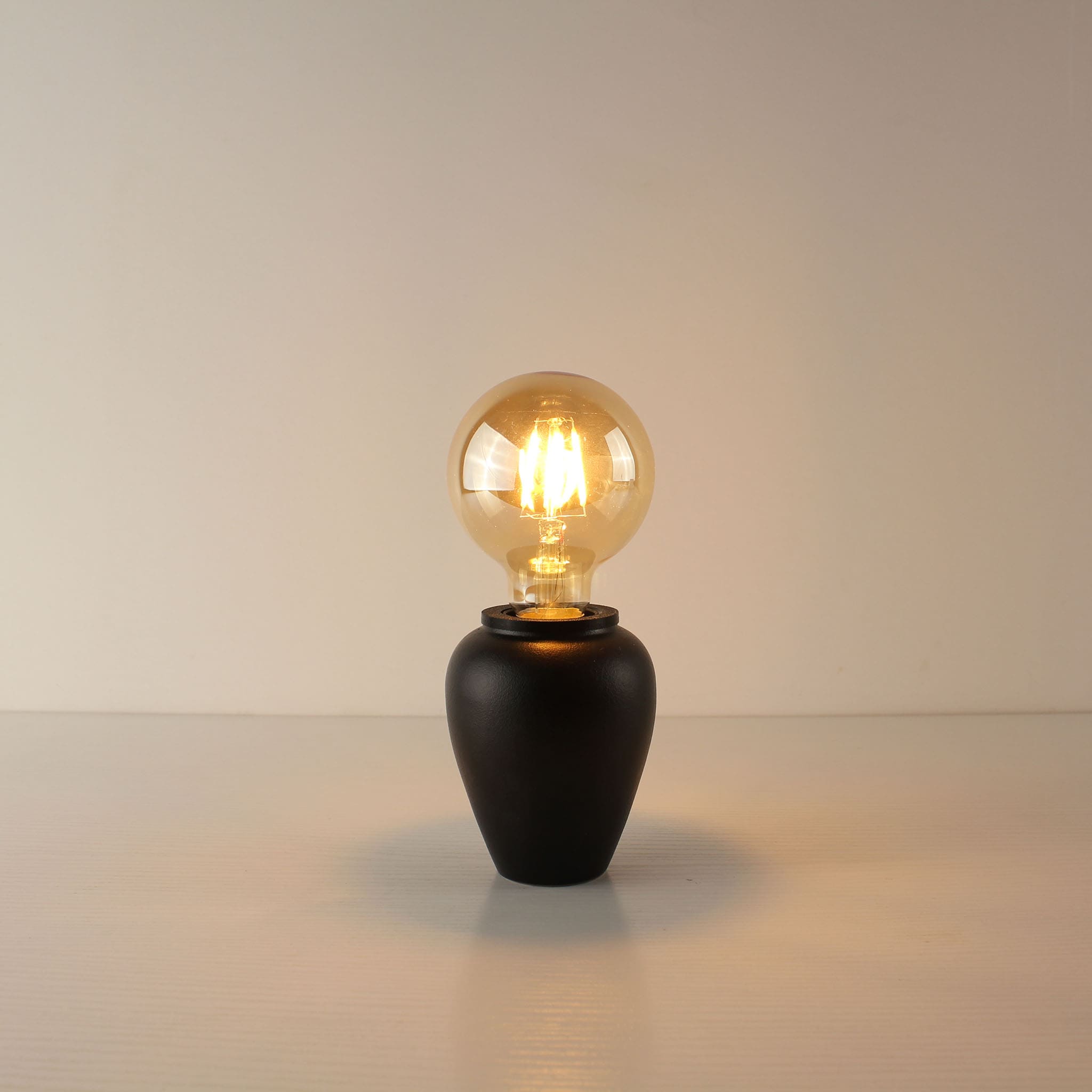 Modern matte black ceramic cordless table lamp with a large spherical A80 vintage Edison bulb, ideal for minimalist home decor