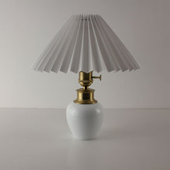 Minimalist white ceramic cordless lamp with a classic white pleated shade and brass toggle switch.