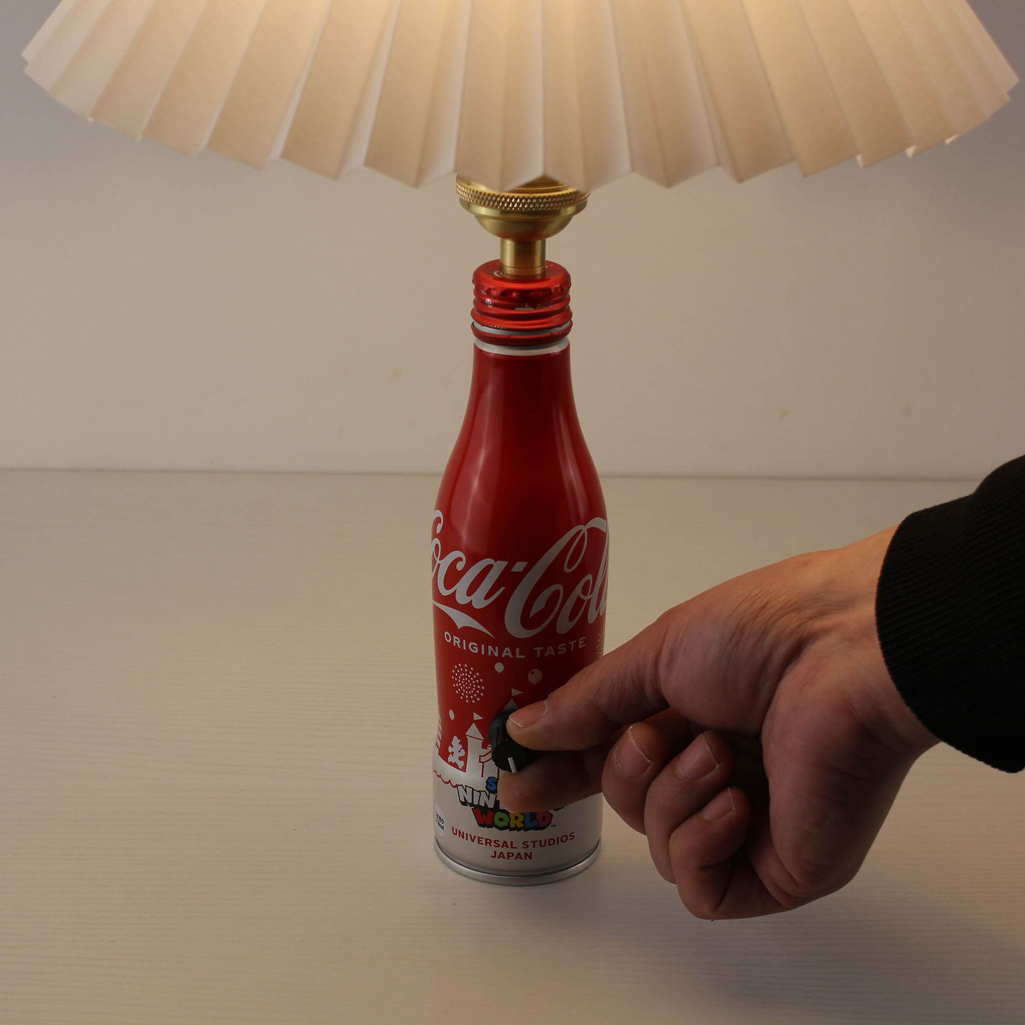 Close-up of a hand turning the mechanical rotary knob on the Nintendo World bottle lamp to adjust brightness from 0% to 100%
