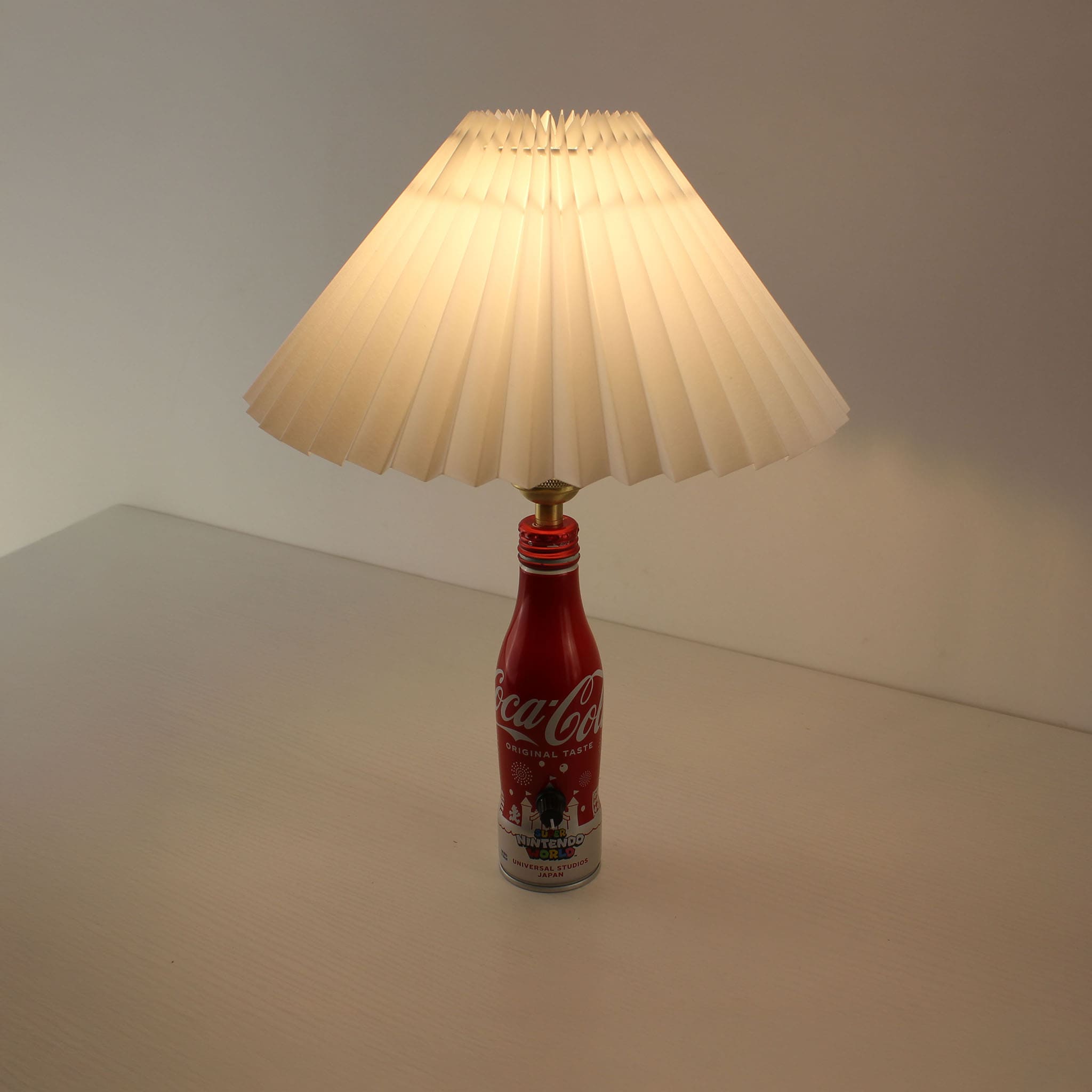 The Super Nintendo World bottle lamp turned on, emitting a warm, inviting glow through its white pleated lampshade