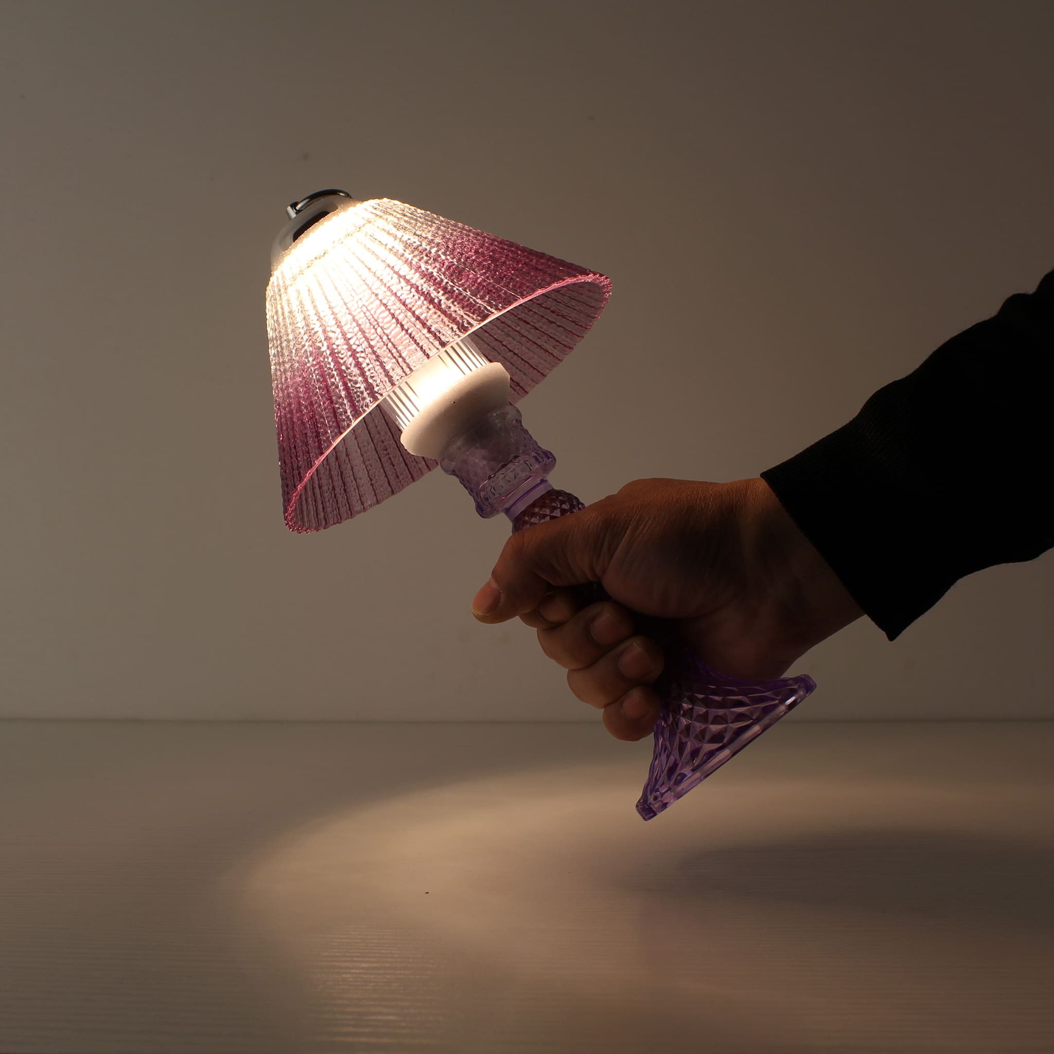 A hand holding the portable cool purple lantern (ON) by its metal ring, demonstrating cordless mobility and 150h battery life.