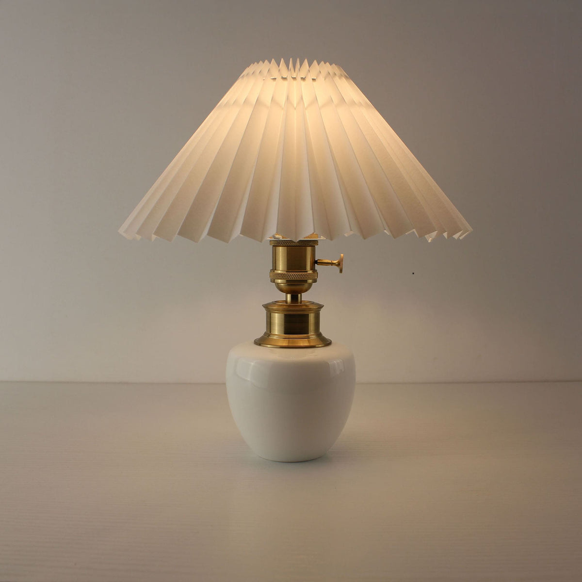 Portable white ceramic lamp with warm glowing light and white pleated shade for bedside.