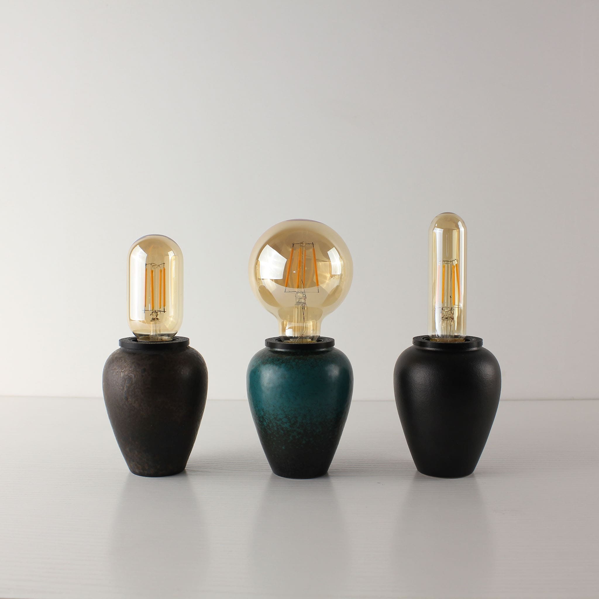 Comparison of three rechargeable ceramic table lamps showing the rust, green, and black tea caddy bases with clear vintage LED bulbs
