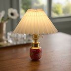 Close-up of a red ceramic cordless table lamp with pleated shade and brass-finish aluminum hardware