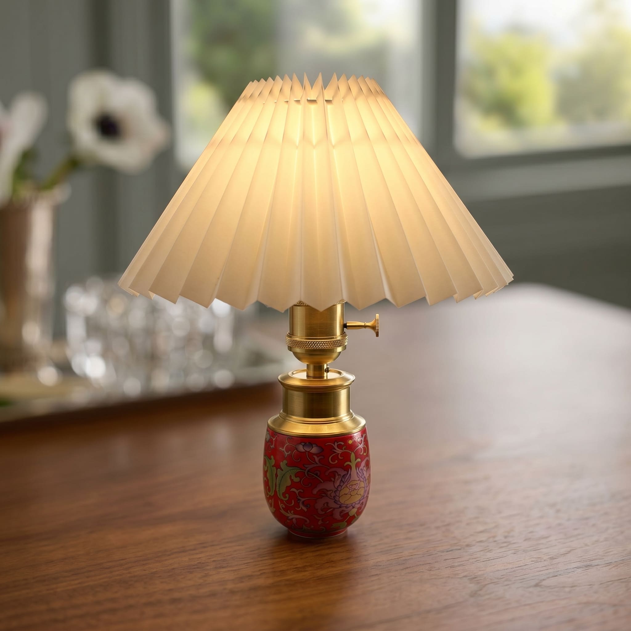 Close-up of a red ceramic cordless table lamp with pleated shade and brass-finish aluminum hardware