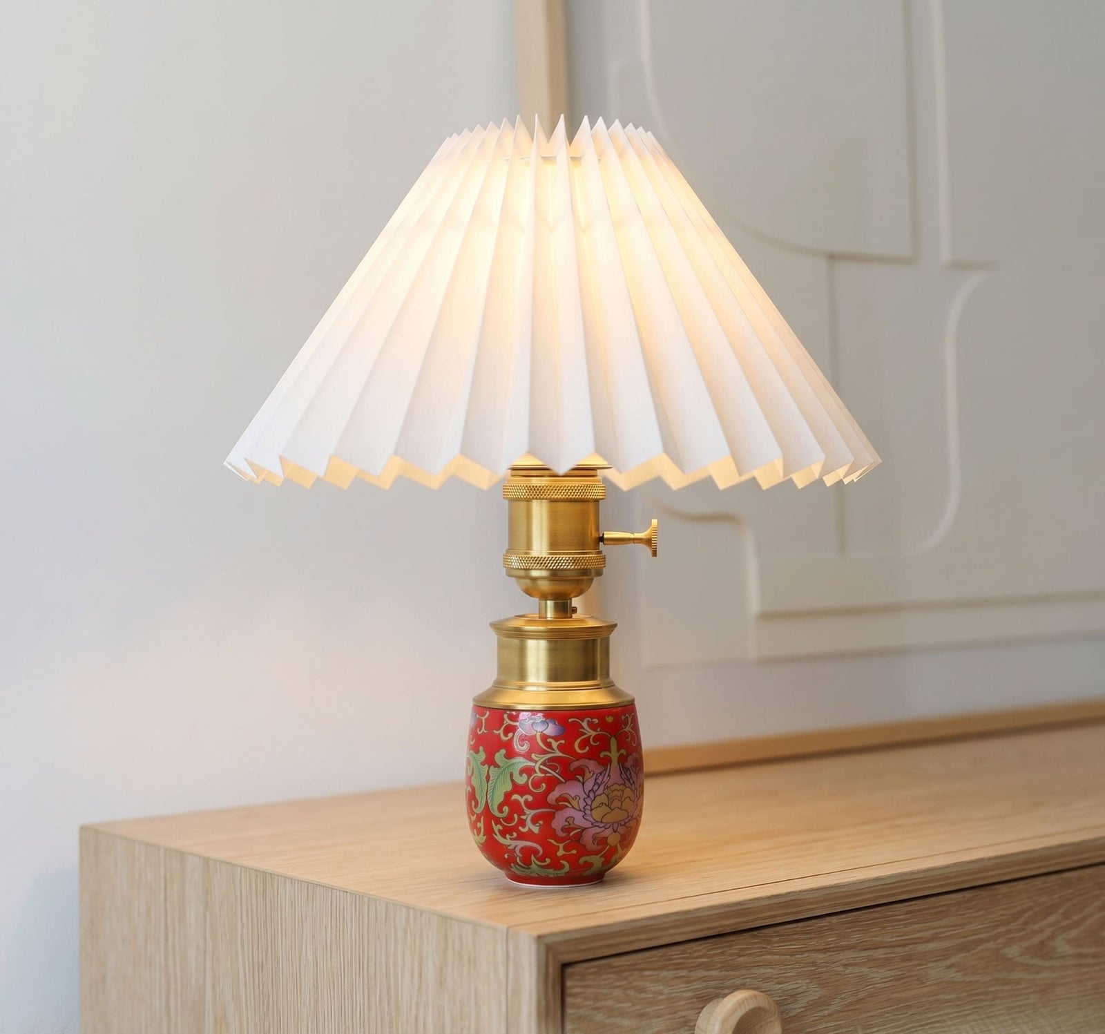 Red ceramic cordless table lamp with a pleated shade on a modern wooden sideboard