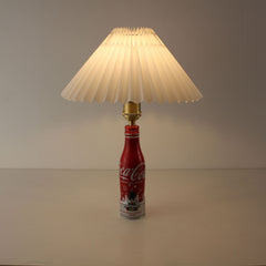 A cordless table lamp made from a red Super Nintendo World Coca-Cola bottle with a white pleated shade, shown in a bright studio setting