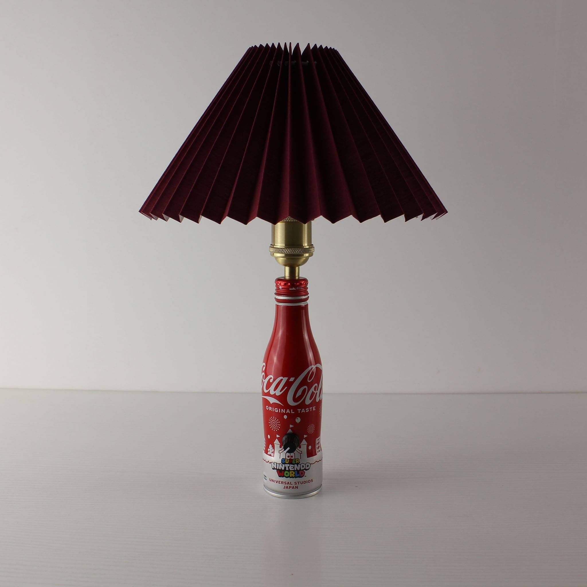An upcycled Nintendo-themed Coca-Cola bottle lamp featuring a premium burgundy (dark red) pleated lampshade