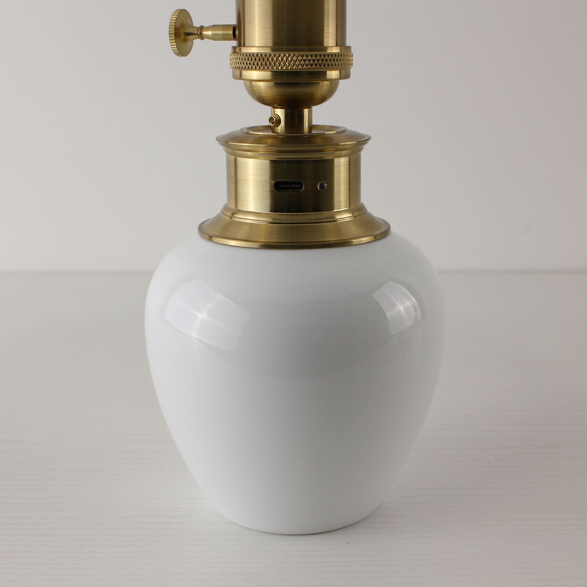 Close-up of the brass hardware on the white porcelain lamp base showing the USB-C charging port and indicator light.