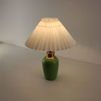 Warm light glowing through the white pleated shade of a green ceramic USB rechargeable lamp, wireless design.
