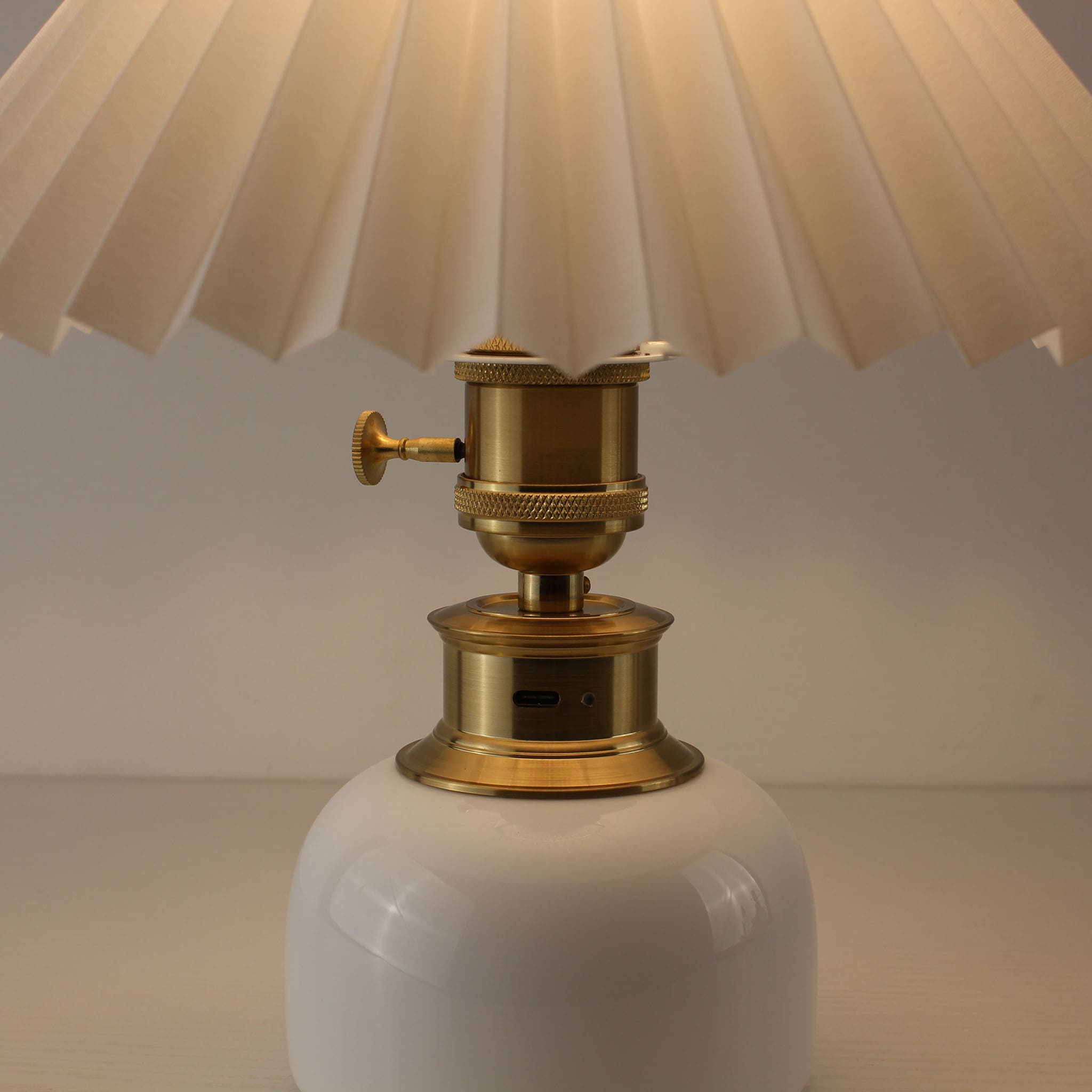 Close-up of the USB-C rechargeable port and brass switch on a white porcelain cordless table lamp.